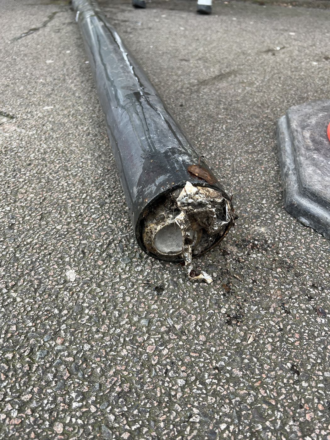 Foot of a cast iron downpipe at pavement level packed with silt and debris
