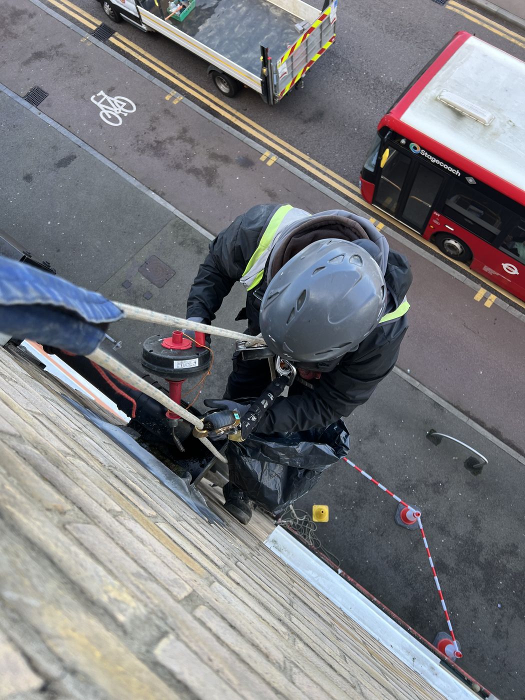 Rope access technician clearing a high level gutter above a London street, footway cordoned below