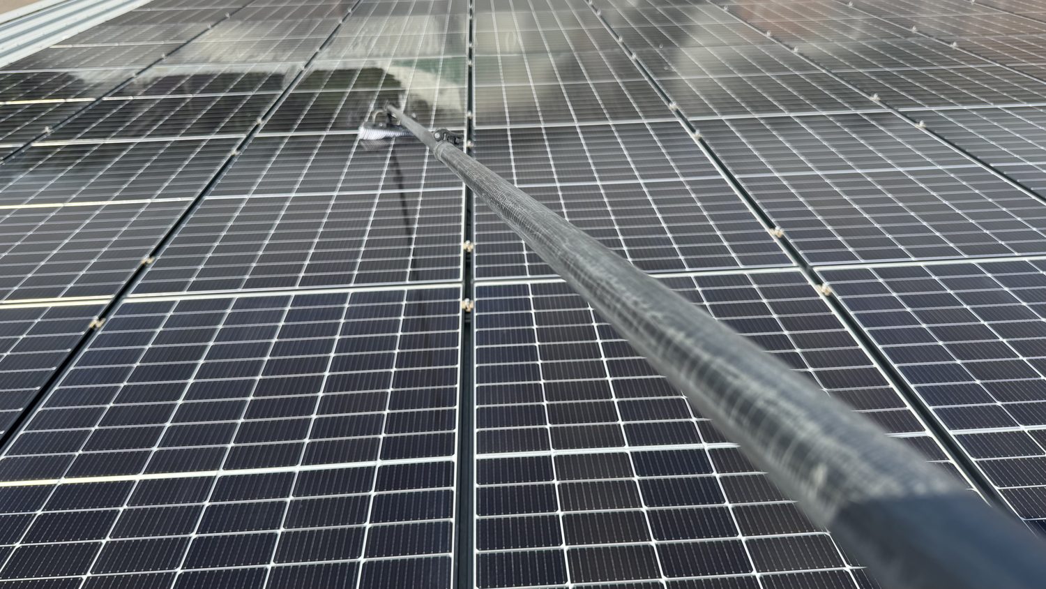 Telescopic water-fed pole reaching across a rooftop solar array from the ridge