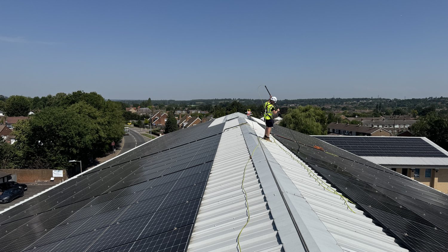 Long industrial roof with solar panels either side of the ridge, technician at the far end