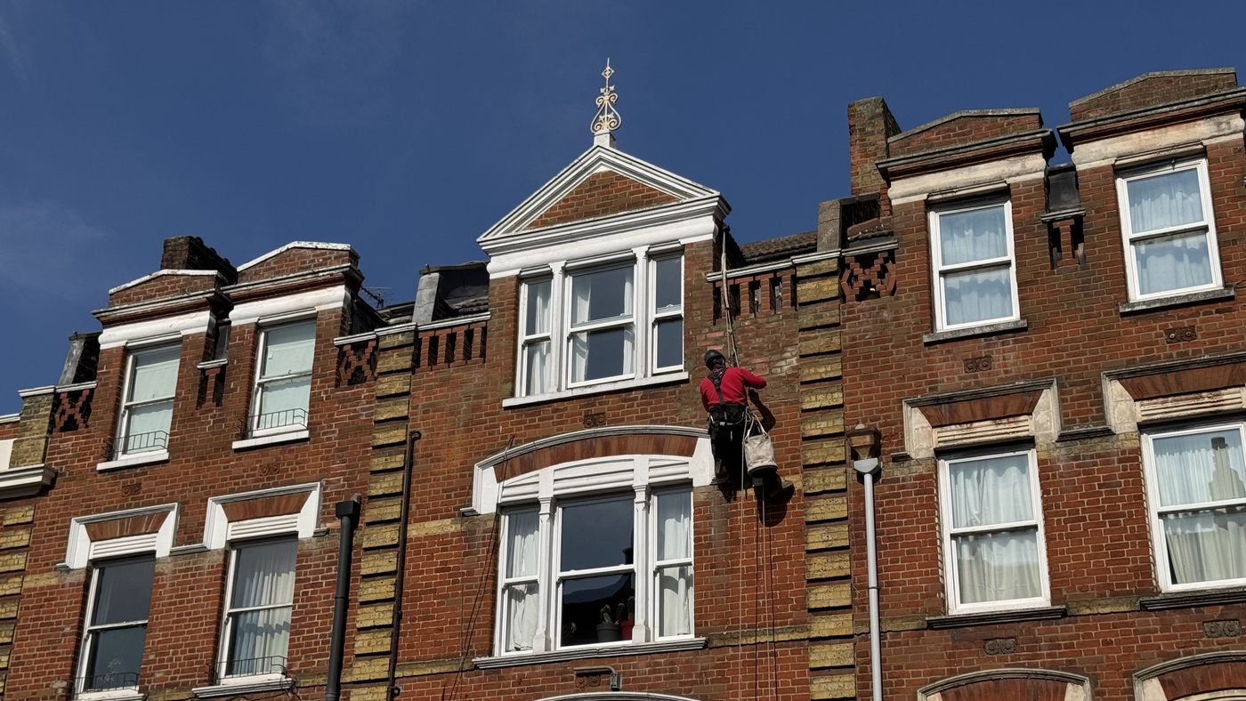 Victorian red brick building on Stoke Newington Church Street with a rope access technician working on the facade