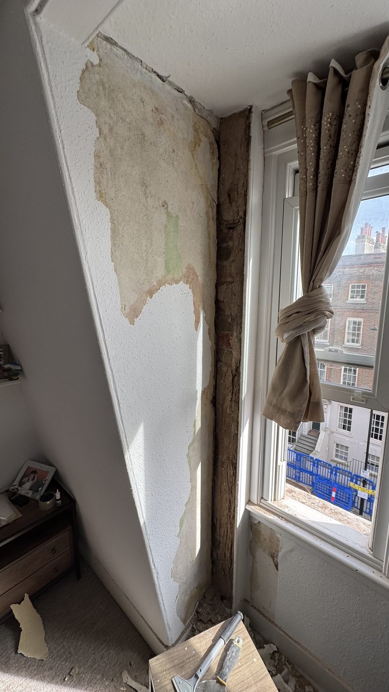Internal window reveal with plaster stripped back showing water staining across the wall