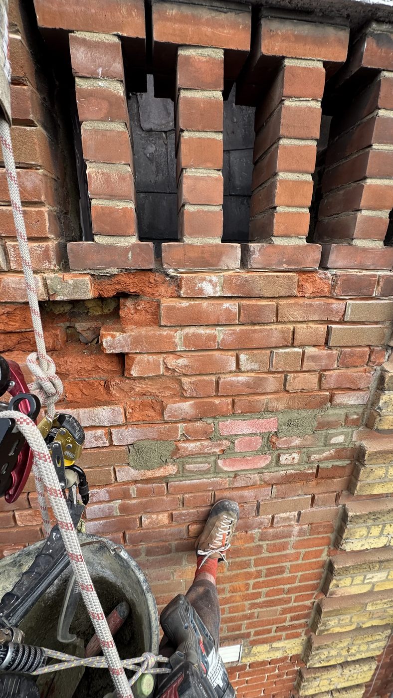 Rope access technician repointing high level brickwork with joints raked out