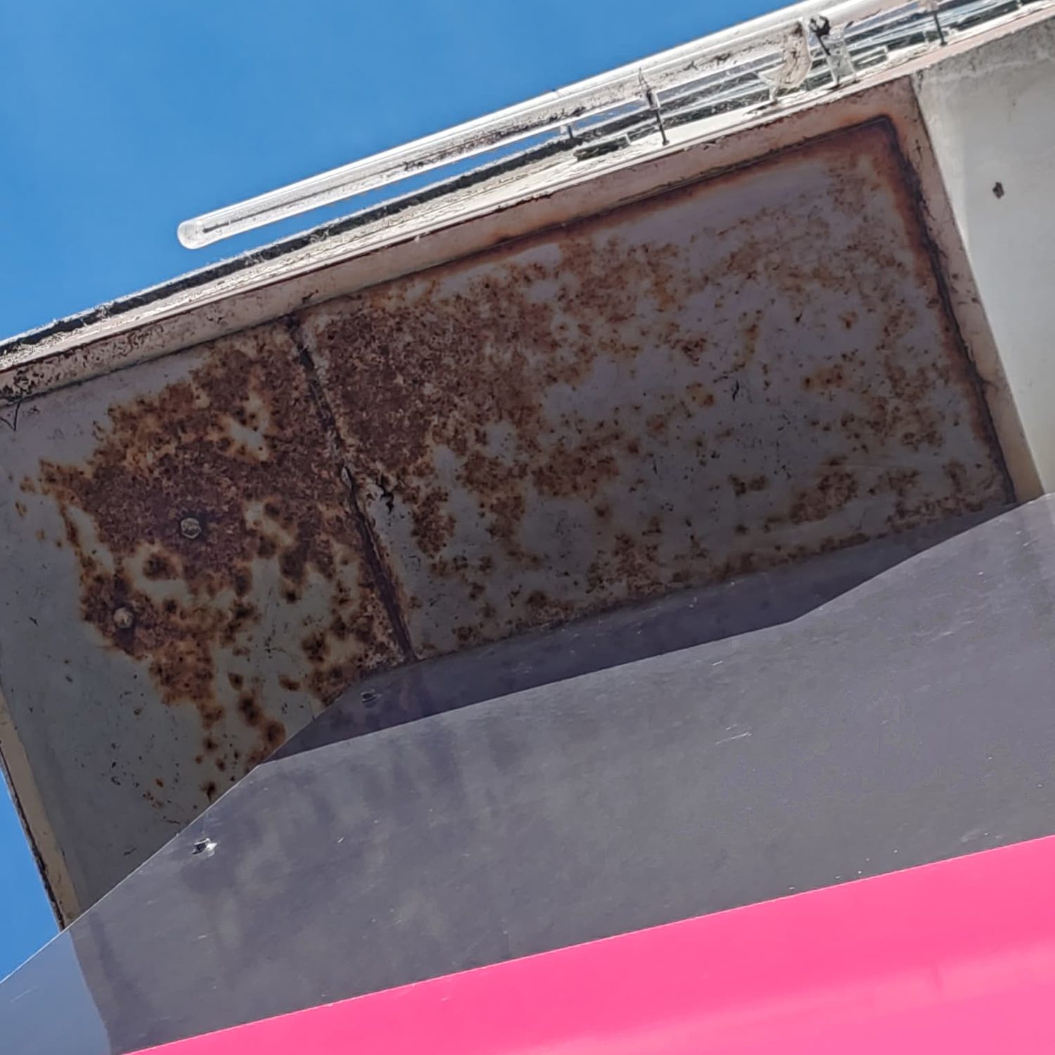 Steel fascia soffit panel with corrosion across its full face above a sign