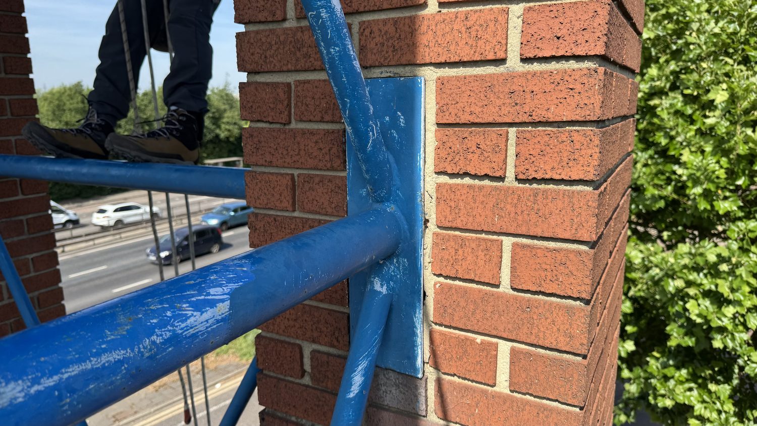 Rope access technician working on blue structural steelwork at height above a road